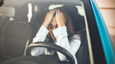 Woman sitting in a car upset with her hands on her face