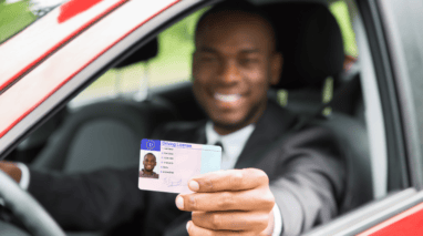 Smiling man sitting on his car holding up his drivers license