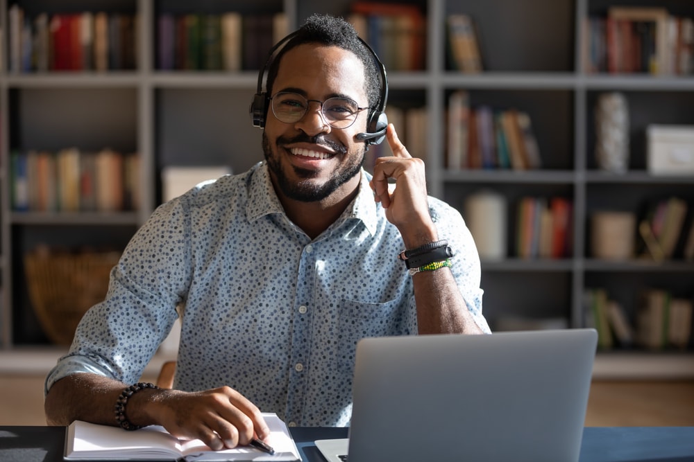 Happy smiling African American insurance agent with headset at desk - selling insurance in niche markets