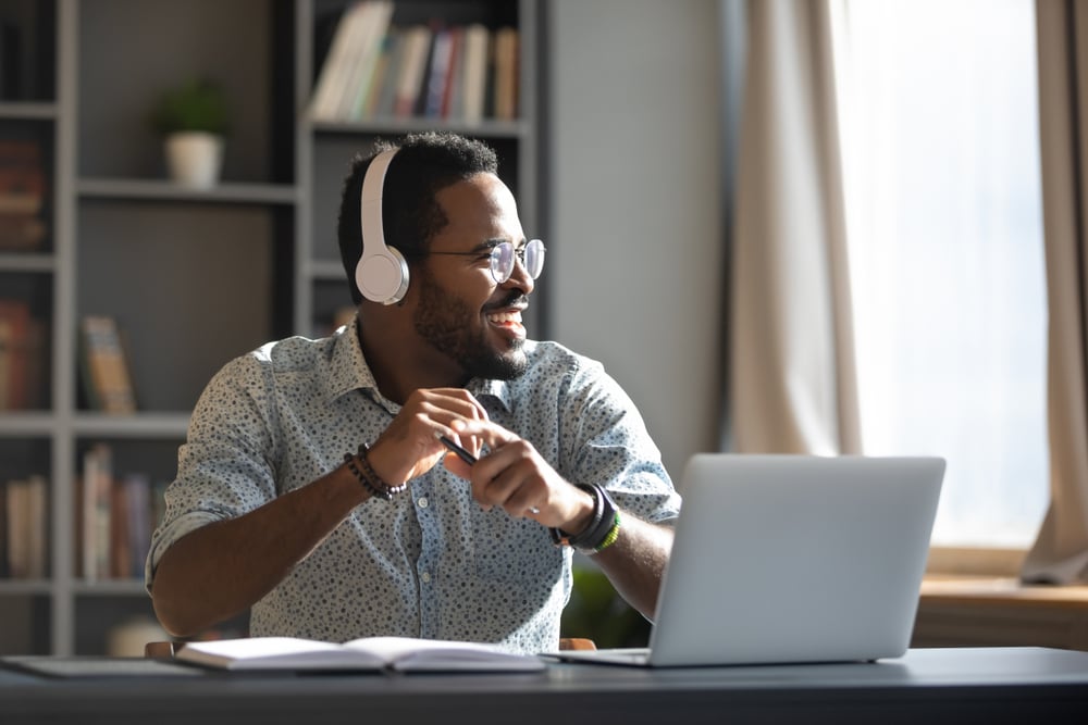 Smiling African-American man listening to podcast at his desk.