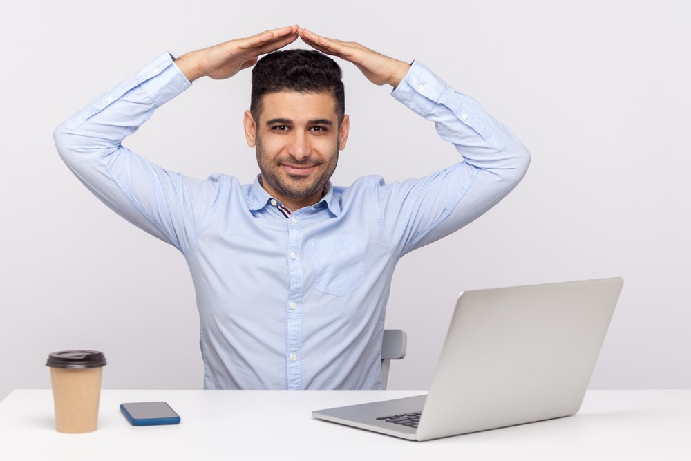 Smiling insurance agent illustartes internet security with hands over head in front of laptop.