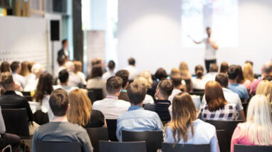 Insurance agents in a conference session listen to a speaker.