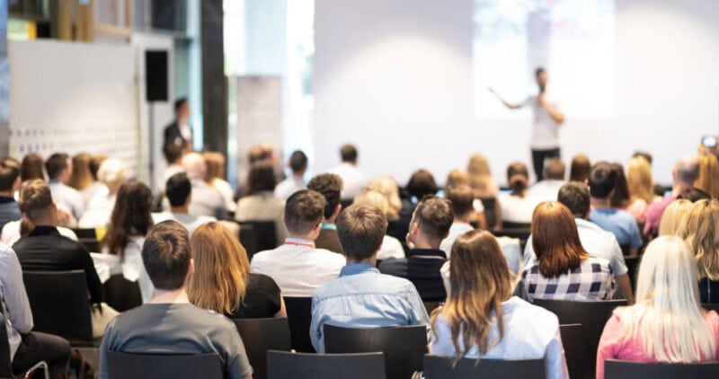 Insurance agents in a conference session listen to a speaker.