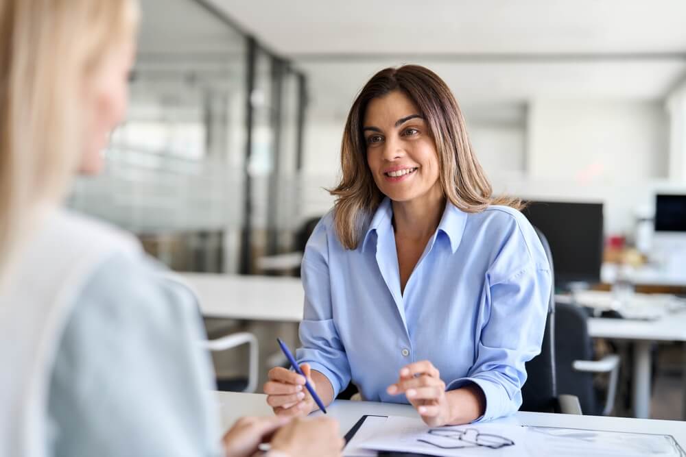 Smiling mature woman at a desk facing an agent.