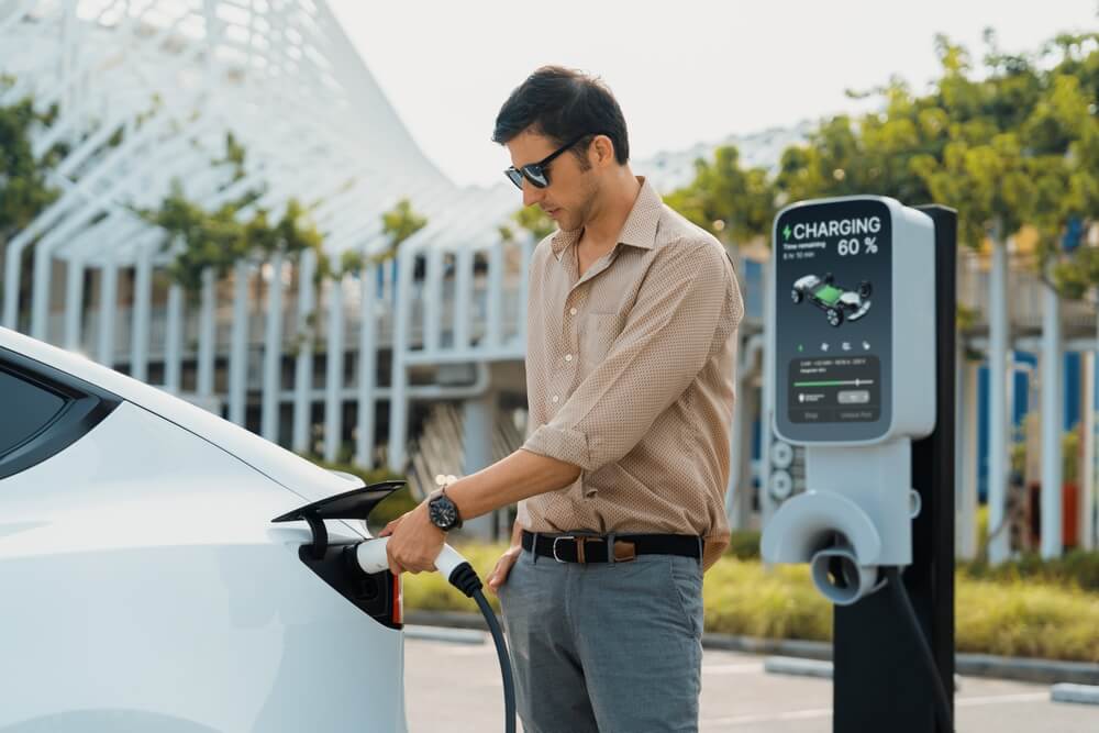 Man at EV charging station charging is car.