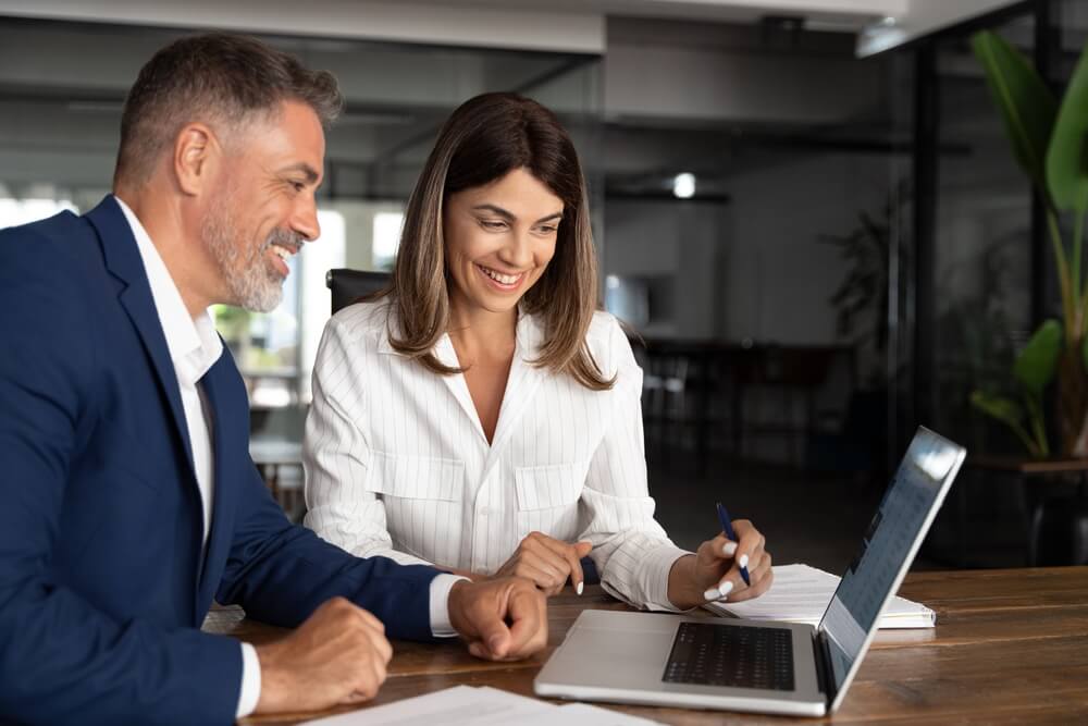 Man and woman business partners work together with a laptop - partner with Bluefire Insurance.